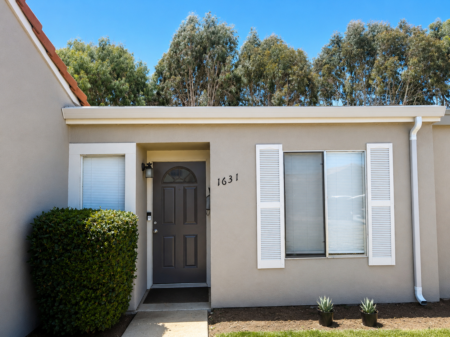 New white gutters and downspout installed at front entry of a stucco home