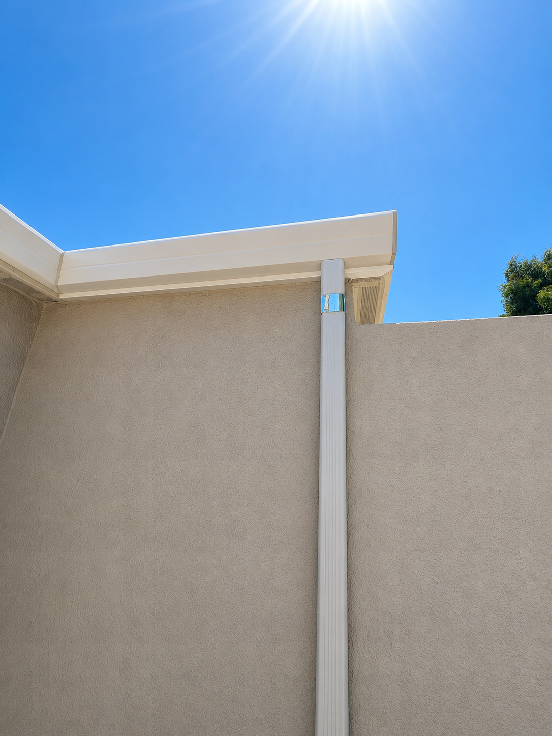 Close-up of white aluminum downspout and seamless gutter at stucco wall corner