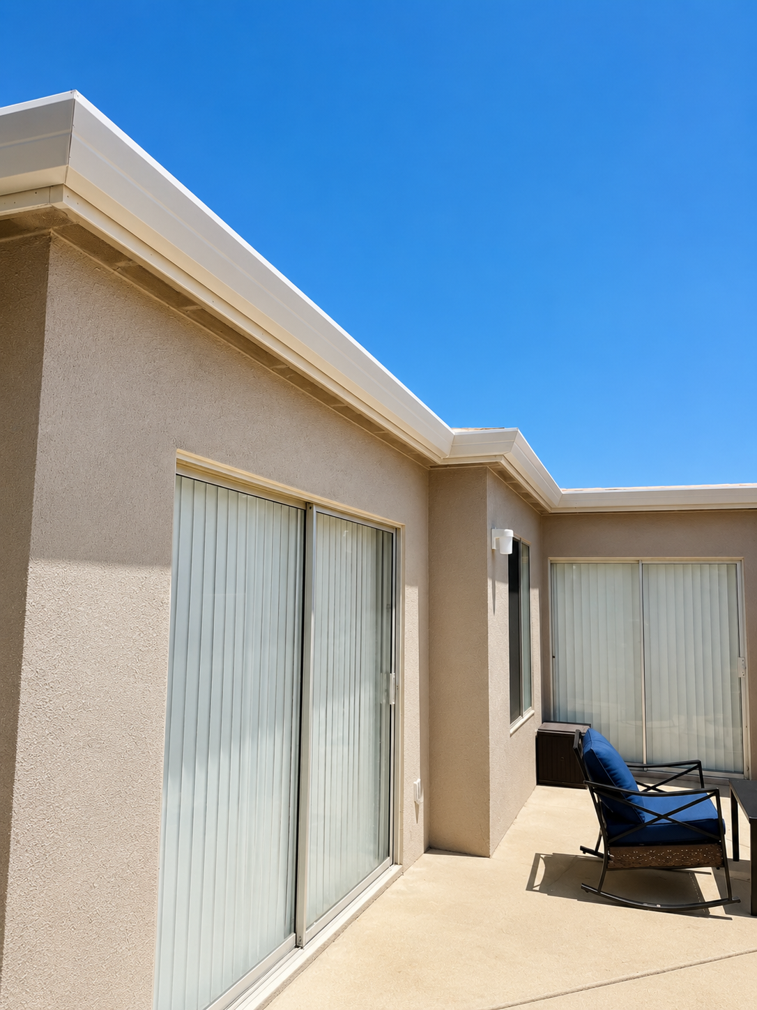 White seamless gutters installed along a stucco patio home with bright blue sky